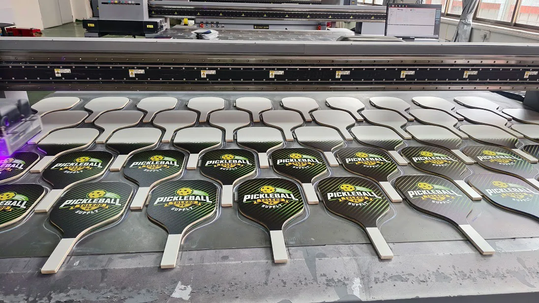 High precision industrial UV printer applying custom brand graphics, logos, and grit texture on paddle face